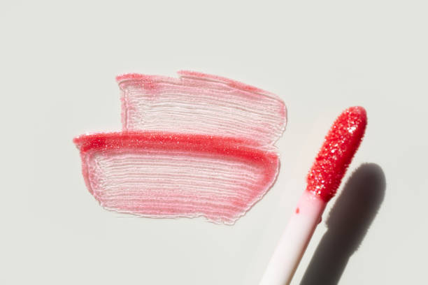 Smears of shining lip gloss and lip gloss brush on white background, hard shadows.