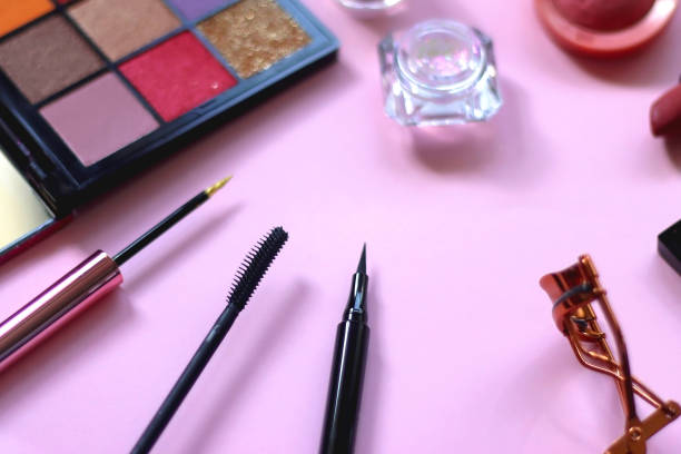 Various colorful make up products on pastel pink background.